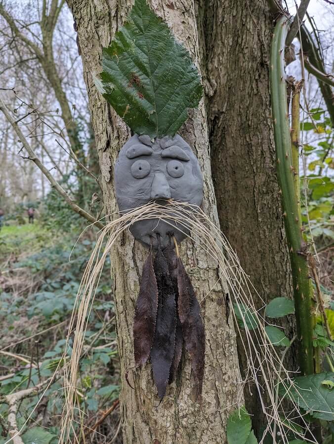 A clay face sculpted onto a tree. Long dried grass makes a moustache.