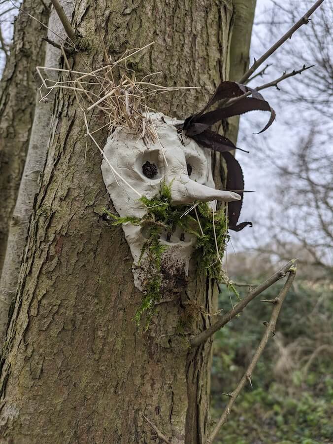A clay face sculpted onto a tree. It has a long nose and a moss beard.