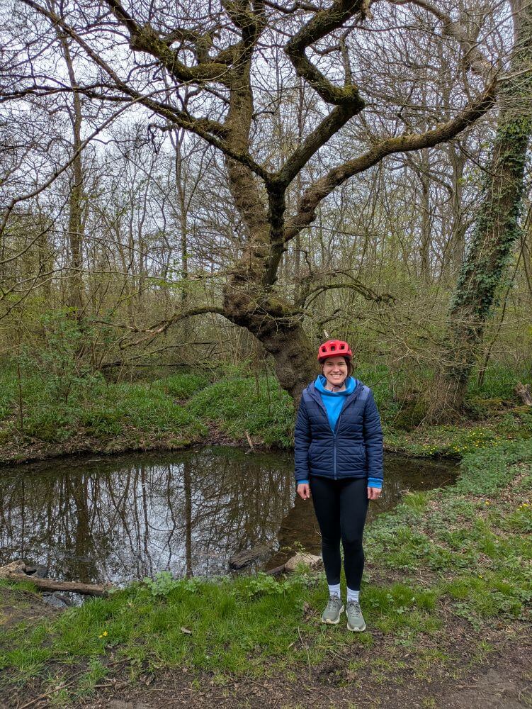 Felicity standing next to her tree which is growing out of a pond.
